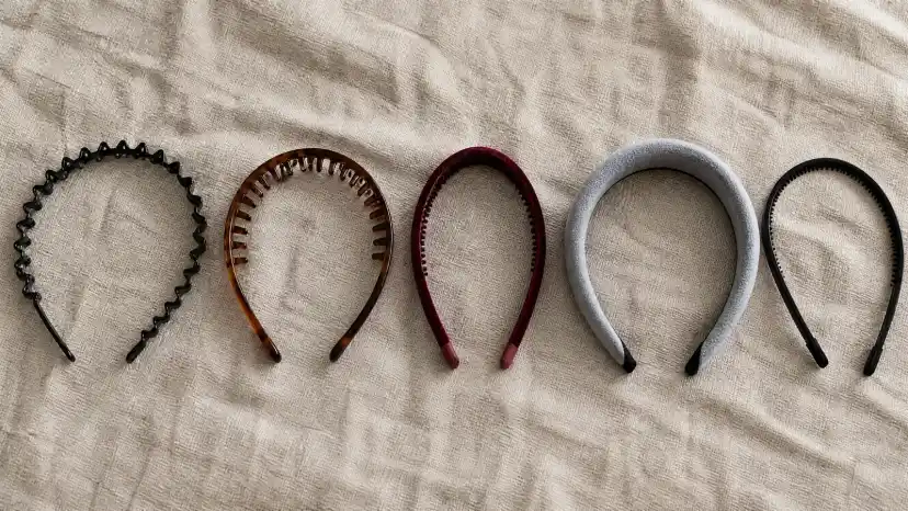 Five non-slip headbands laid in a row on linen: a black zig-zag band, a tortoiseshell silicone comb band, a wine-red velvet band with teeth, a wide padded grey band and a slim black toothed band